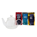 Clear glass teapot with three packages of tea on a white background