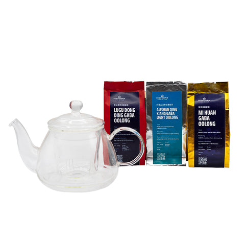 Clear glass teapot with three packages of tea on a white background